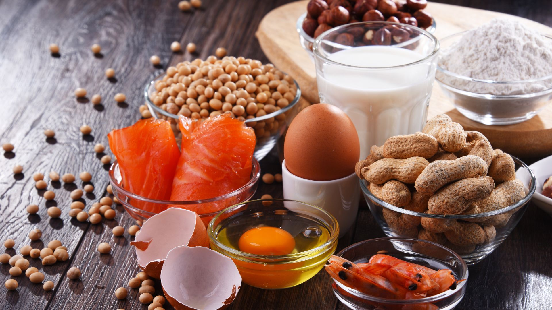 common food allergens sit on a dark wooden table as a group including salmon egg milk peanuts shrimp and other allergen food